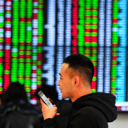 A man talks on his mobile phone with big screen showing stock prices behind at a stock brokerage house in Shenyang. Photo:: China Photo Press