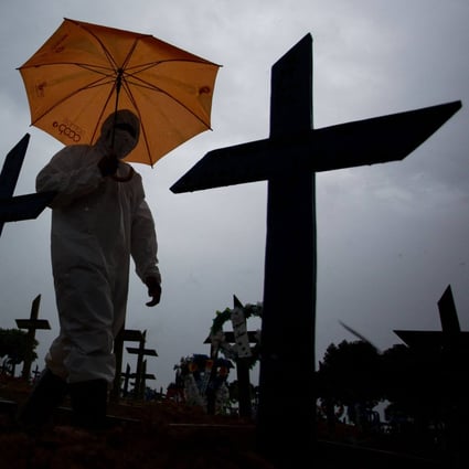 A worker wearing a protective suit and carrying an umbrella walks past the graves of Covid-19 victims at a cemetery in Manaus, Brazil in February 2021. Photo: AFP