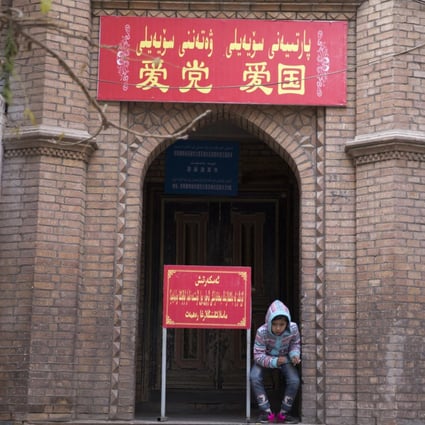 A child rests near the entrance to a mosque where a banner  reads “Love the party, Love the country” in Kashgar in Xinjiang.  Photo: AP 