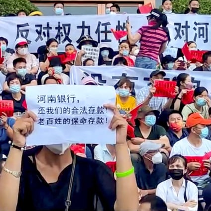 On Sunday, July 10, demonstrators hold up signs protesting against the freezing of deposits by some rural-based banks, outside a People’s Bank of China building in Zhengzhou, Henan province. The text in the foreground reads, “Henan Bank, return to us our legal deposits! The people’s life-saving deposits!” Photo: Reuters