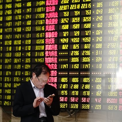 A man looks at his smartphone in front of a screen showing stock prices in a brokerage house in Shanghai. Photo: AP