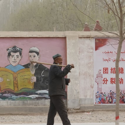 A farmer walks past murals and posters depicting ethnic minority residents studying the constitution with slogans reading “Unity and stability is fortune, separatism and turmoil is misfortune” near Kashgar, Xinjiang, on March 19, 2021. Photo: AP