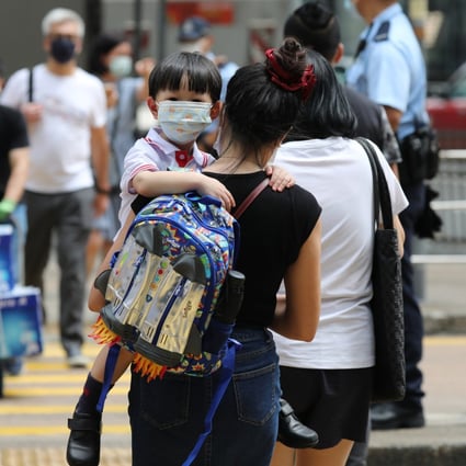 A child wearing a mask is carried by an adult as they cross the road in Central. If the vaccine pass scheme is expanded to include young children, it will impose a burden on low-income families having to buy smartphones for children. Photo: Nora Tam