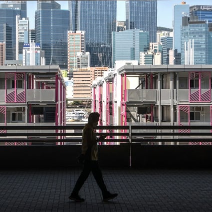 Skyscrapers can be seen behind an isolation facility in Kai Tak as a man passes in a mask, on June 28. Photo: Bloomberg