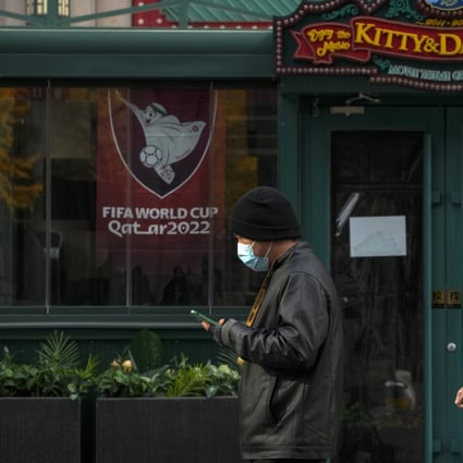 People wearing face masks walk by a closed restaurant displaying World Cup posters. Photo: AP