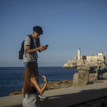 A youth uses his smartphone as he and a friend walk along the Malecon seawall in Havana, Cuba, on November 25, 2022. Ever-widening access to the internet is offering a new opportunity for Cubans looking for hard-to-obtain basic goods: online shopping. Photo: AP