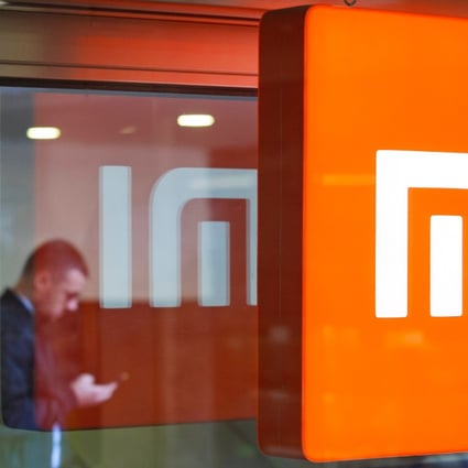 A man looks at his smartphone next to a reflected Xiaomi logo. Photo: Shutterstock