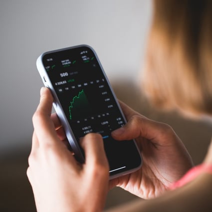 Stock market investor holding a phone investment app index growth chart. Photo: Shutterstock 
