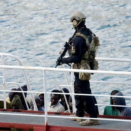 An armed policeman stands guard over migrants from the El Hiblu 1 tanker in Valletta's Grand Harbour on Thursday. Photo: AFP