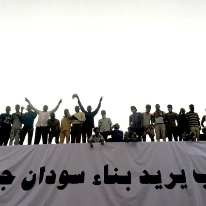 Demonstrators outside the military headquarters in Khartoum, stand above a banner reading in Arabic: ‘People want to build new Sudan’. Photo: Reuters