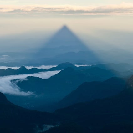 At sunrise on Adam’s Peak, or Sri Pada, in Sri Lanka, the triangular shadow of the mountain is projected across the forest and countryside in the distance. Photo: Alamy