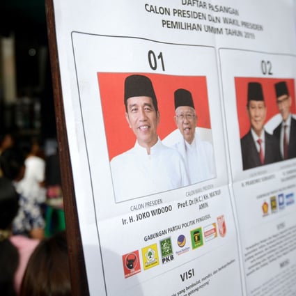 Indonesians wait next to a poster of presidential candidates at a polling centre. Photo: AFP