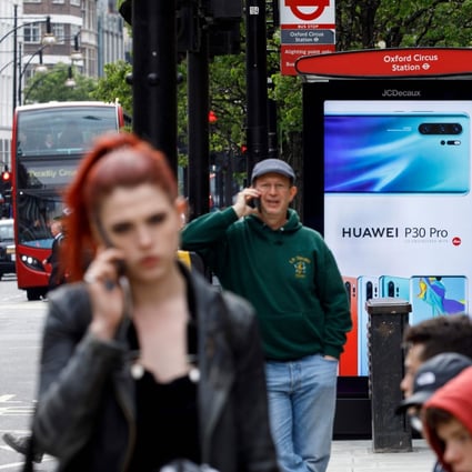 Pedestrians on their mobile phones near a Huawei advertisement at a bus stop in central London in April. Photo: AFP