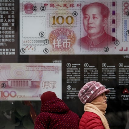 Women walk by a bank window panel displaying the security markers on the latest 100 yuan notes in Beijing. Photo: AP