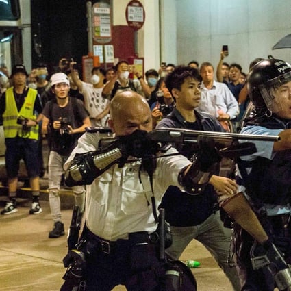 Sergeant Lau Chak-kei points his shotgun at protesters who had gathered outside Kwai Chung Police Station. Photo: AFP