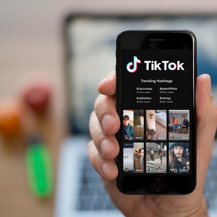 A man looks at his iPhone which displays the Tik Tok logo