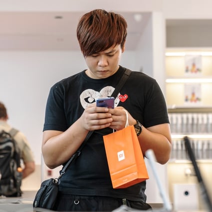 A customer holding a Xiaomi Corp-branded shopping bag uses a smartphone inside a Xiaomi store in Hong Kong on July 6, 2018. Photo: Bloomberg