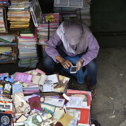 A book vendor in Jakarta uses her mobile phone while waiting for customers. Indonesia has one of the fastest growing internet penetration rates in the region. Photo: AFP