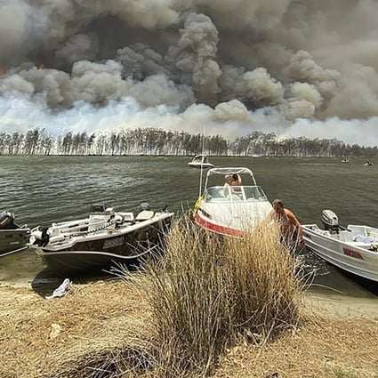 Boats are pulled ashore as smoke and wildfires rage behind Lake Conjola, Australia on Thursday. Photo: AP