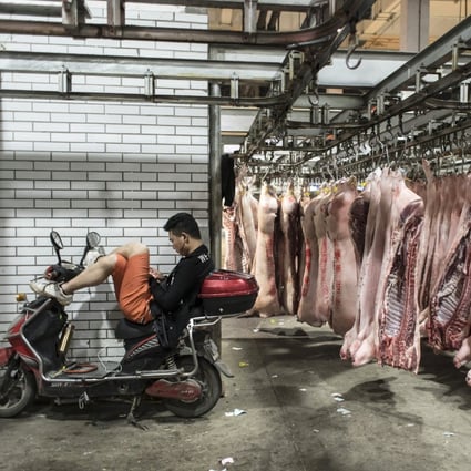 A man sits on a motorcycle next to pig carcasses hanging from a conveyor at a pork wholesale market on the outskirts of Shanghai on May 28, 2019. The US pork industry has been hard hit by Chinese tariffs during the trade war. Photo: Bloomberg