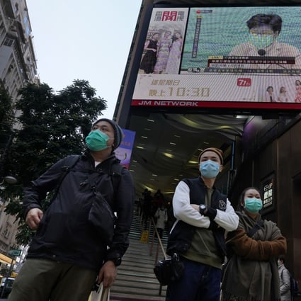 People wearing protective face masks walk around Hong Kong’s shopping areas while a TV screen broadcasts measures to counter the coronavirus outbreak. Photo: AP