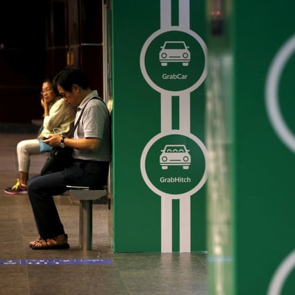 Commuters wait next to advertisements of Grab’s transport booking service app at a railway station in Singapore. Photo: Reuters