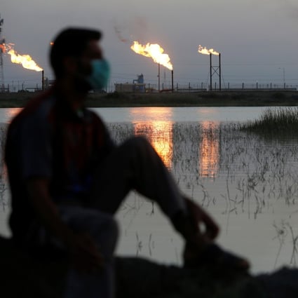 A man wearing a face mask is flanked by flare stacks at the Nahr Bin Umar oilfield, north of Basra, Iraq, on March 9, 2020. Photo: Reuters