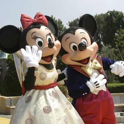 Employees in Mickey and Minnie Mouse costumes wave in front of the Sleeping Beauty Castle at Disneyland in Anaheim, California, in July 2005. Photo: AFP