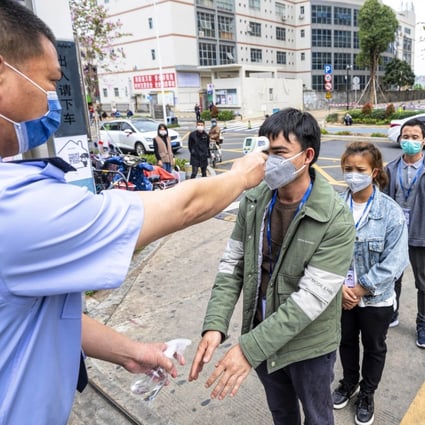 A security guard checks employees body temperature and disinfects their hands at the entrance to a factory in Shenzhen. Photo: EPA-EFE