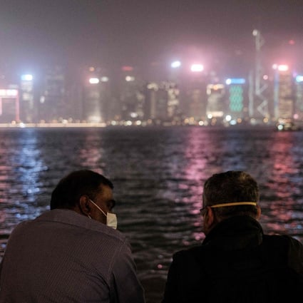 Two men in face masks chat while standing on a Kowloon promenade overlooking Victoria Harbour and the skyline of Hong Kong Island. Photo: AFP