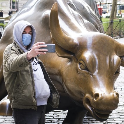 A man in a protective mask takes a selfie with the Charging Bull statue in New York. US markets rallied on Thursday after the Federal Reserve took steps to boost liquidity. Photo: EPA-EFE