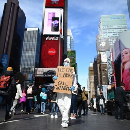 A man wearing a hazmat suit and a mask holds a sign: “The end is near. Call grandma”, at Times Square in New York on March 14. Photo: AFP
