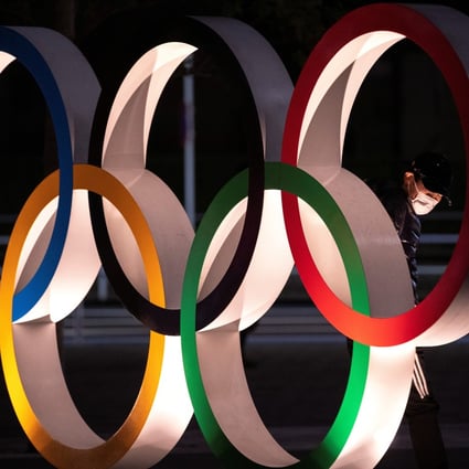 A man wearing a protective face masks looks to The Olympic rings in front of the Japan Olympics Museum in Tokyo. Photo: Reuters