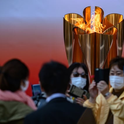 People wearing face masks take pictures in front of the Tokyo 2020 Olympic flame. Photo: AFP