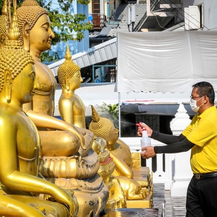 A volunteer disinfects Buddha statues before a televised anti-plague prayer at Wat Traimit Temple, Bangkok, amid lockdown restrictions to contain the spread of the coronavirus. Photo: AFP