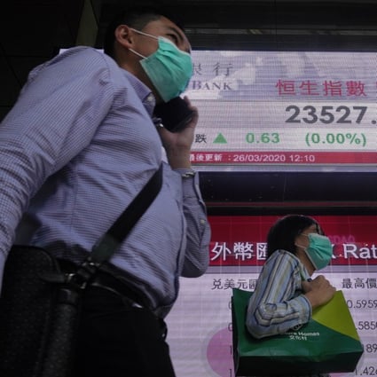 People wearing face masks walk past an electronic board displaying the Hang Seng Index price on March 26, 2020. Photo: AP