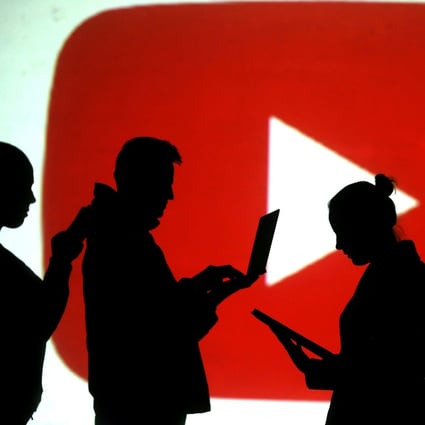 Silhouettes of laptop and mobile device users are seen next to a screen projection of YouTube’s logo in this picture illustration. Photo: Reuters/Dado Ruvic