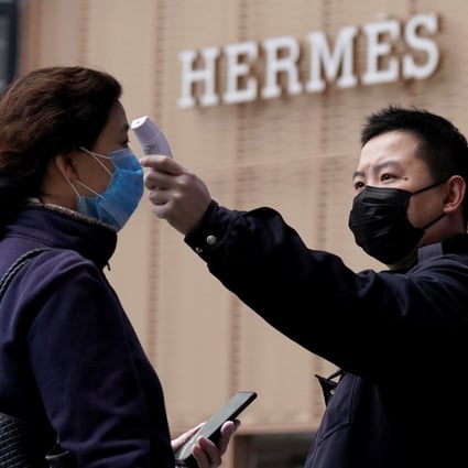 A management staff member measures the body temperature of a woman entering a shopping mall near a Hermès store in Wuhan, Hubei province, the epicentre of China’s coronavirus outbreak. Photo: Reuters