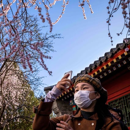 A woman wearing a face mask amid concerns over the spread of the novel coronavirus takes a photograph with her smartphone at a park in Beijing on March 14, 2020. Photo: AFP