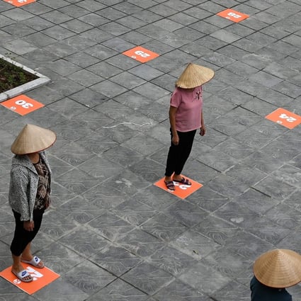 Residents wearing face masks practice social distancing as they wait in a queue for free rice in Hanoi. Photo: AFP