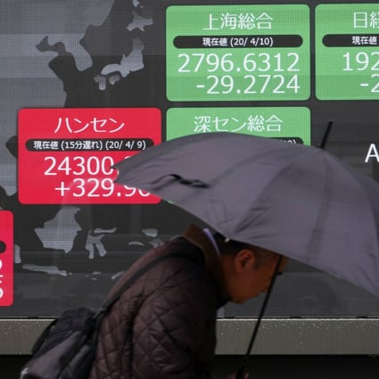 A man walks in the rain past an electronic stock board showing Japan's Nikkei 225 and other Asian countries' stocks at a securities firm in Tokyo on April 13, 2020. Photo: Associated Press