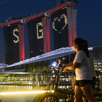 People walk by with their bicycles as Marina Bay Sands lights up with a message of hope on April 10, 2020. Photo: AFP