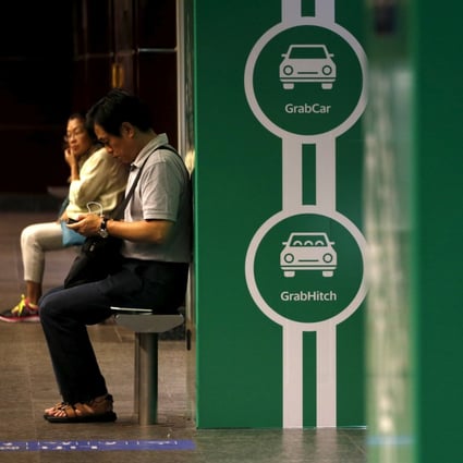 Commuters wait next to Grab’s transport booking service app advertisements at a railway station in Singapore in February of 2016. Photo: Reuters