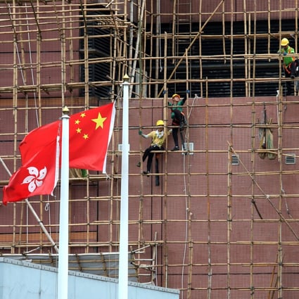 Construction workers remove the scaffolding on a building in Sham Shui Po as the Hong Kong and Chinese flags flutter in the foreground, in June 2019. Photo: Felix Wong