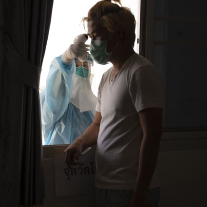 A Thai Ministry of Public health official takes a man’s temperature through a window at the barracks of the Royal Thai Air Force Flight Training School, serving as a state coronavirus quarantine facility for Thai citizens returning from overseas. Photo: Charles Dharapak