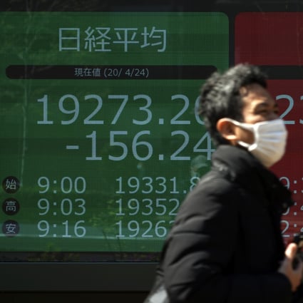 A man wearing a mask twalks past an electronic stock board showing Japan's Nikkei 225 and New York Dow indexes at a securities firm in Tokyo. Stocks in Asia-Pacific region are rising on the back of measures to reboot economies. Photo: AP