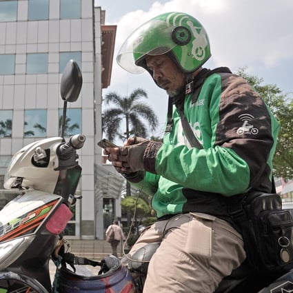 A Go-Jek motorcycle driver checks his smartphone, while preparing for another delivery in Jakarta, Indonesia. Gojek managers pledged to funnel 25 per cent of their salaries over the next year into a fund designed to support drivers, merchants and partners, following the company’s decision to cut 430 jobs. Photo: Bloomberg