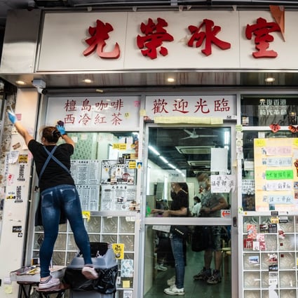 An employee scrapes off stickers and posters with messages in support of the protest movement on a wall outside a restaurant in Hong Kong. Photo: Bloomberg