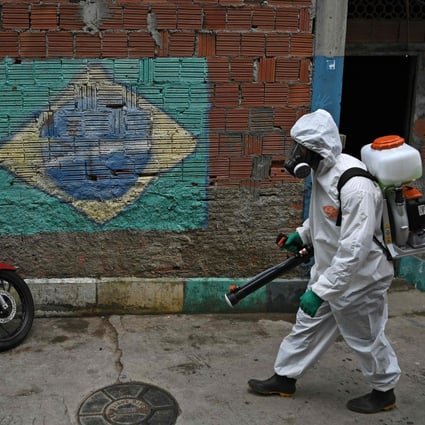 A volunteer walks past a mural of the Brazilian flag as he disinfects an area at the Babilonia favela, in Rio de Janeiro. Photo: AFP