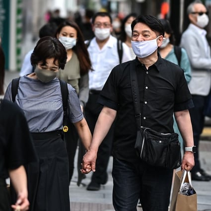 People wearing face masks walk in a street in Tokyo on July 20, as Japan’s death toll eclipsed 1,000, and 168 new cases were recorded in the capital. Photo: AFP